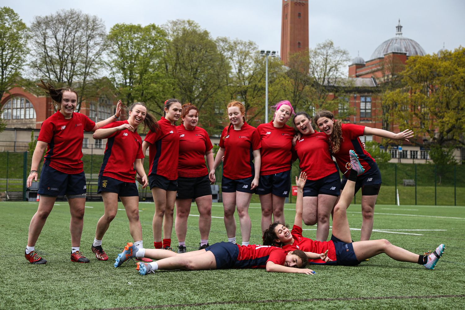 Sports team in red uniforms posing for fun group photos on a grass field.