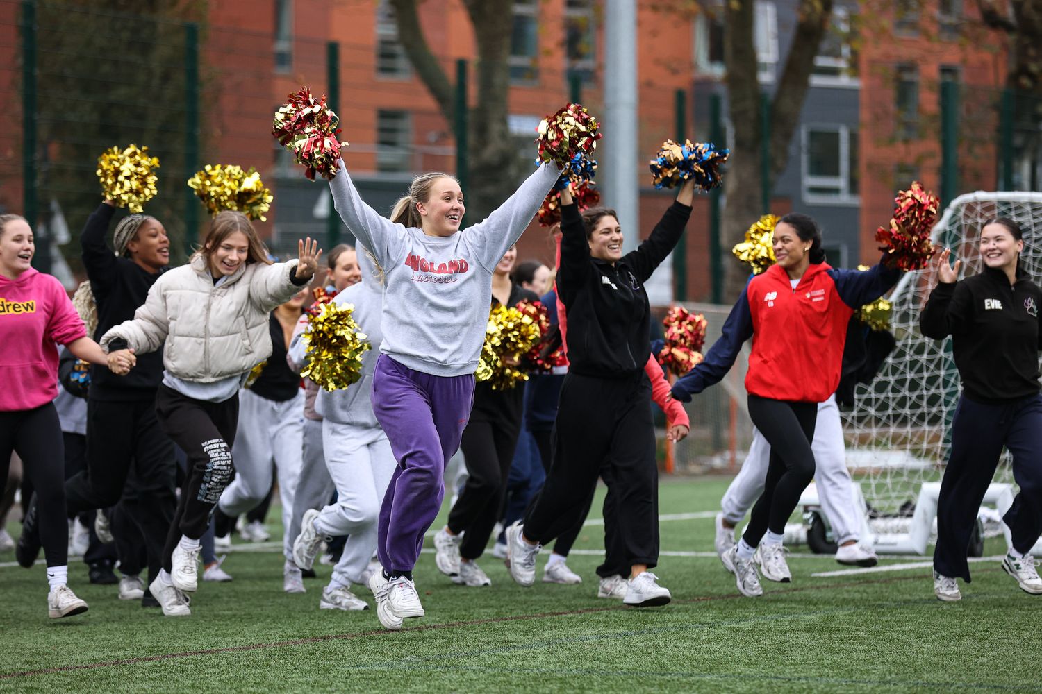 A group of cheerleaders in white uniforms perform synchronized jumps during an outdoor routine on a field.