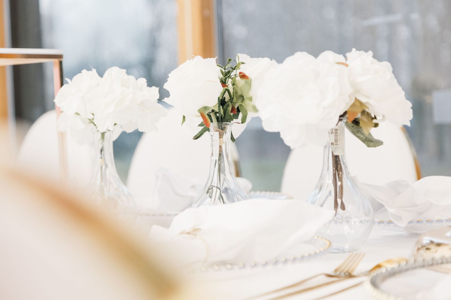 White flower centerpieces in glass vases arranged on elegant table setting.