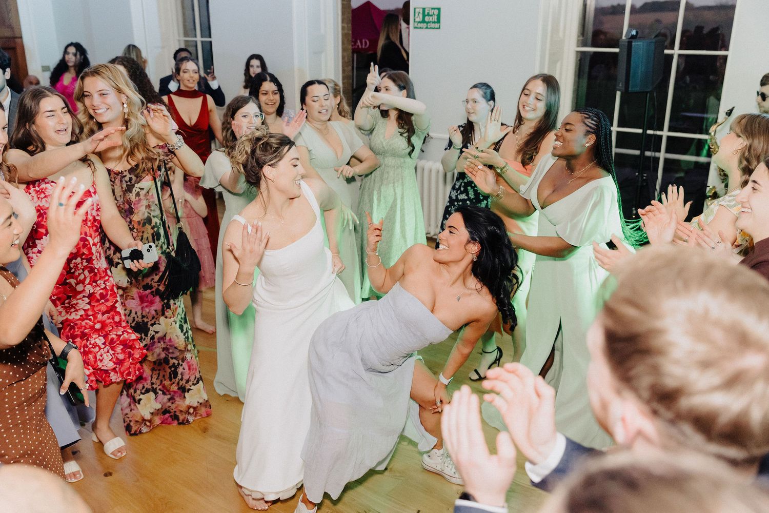 Bride dancing joyfully with bridesmaids in sage green dresses at a lively wedding reception celebration.