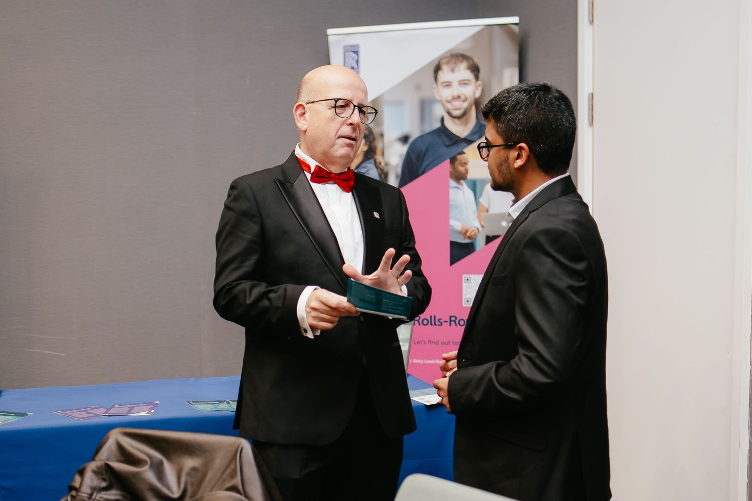 Two people in formal attire shake hands and exchange documents during a business meeting.