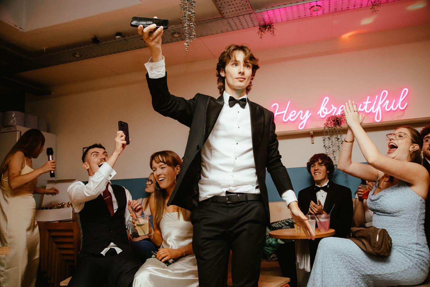 Wedding guests dancing and celebrating under pink lighting at reception party.