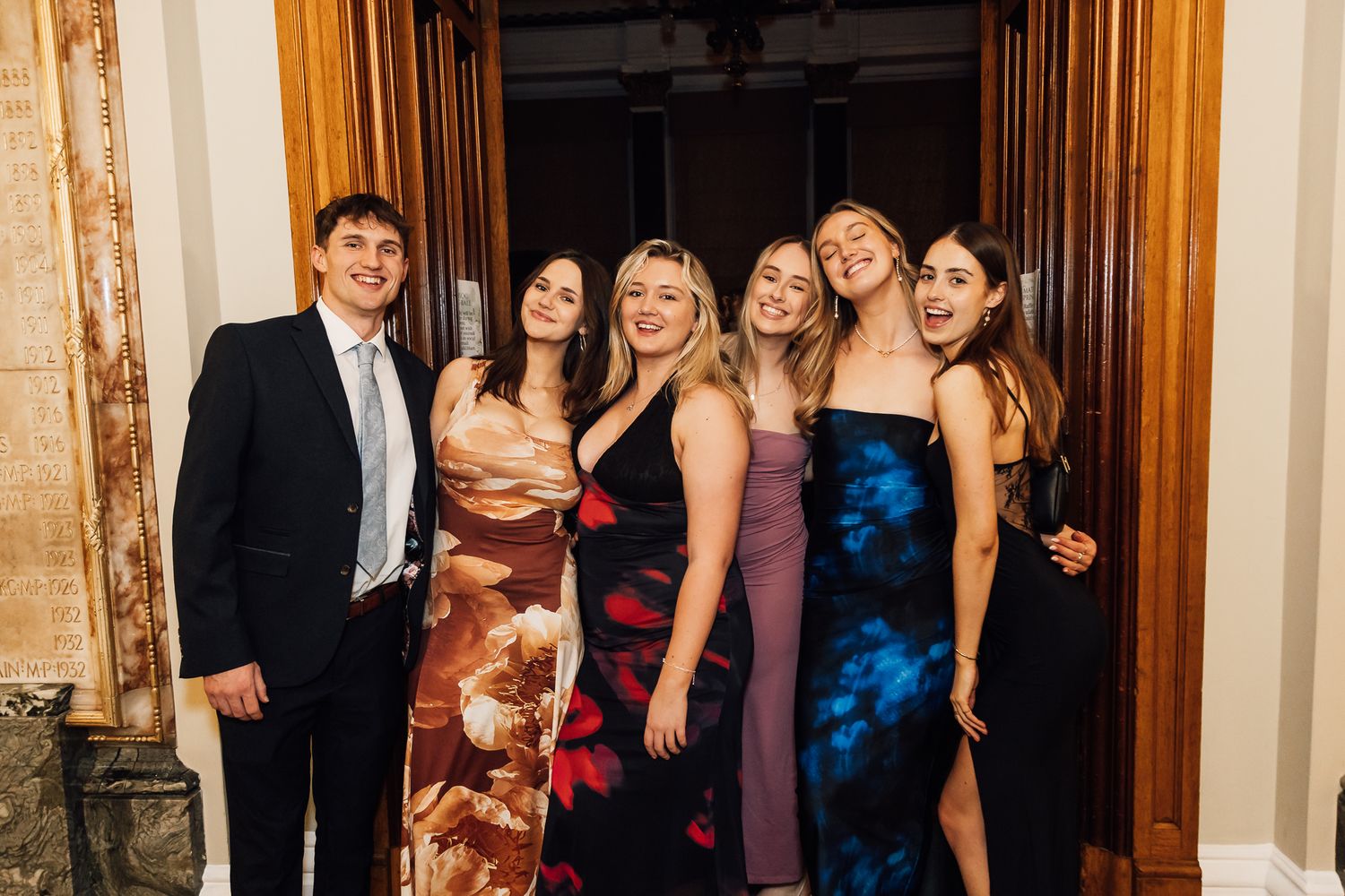 Wedding party guests pose together in formal attire inside an elegant venue.