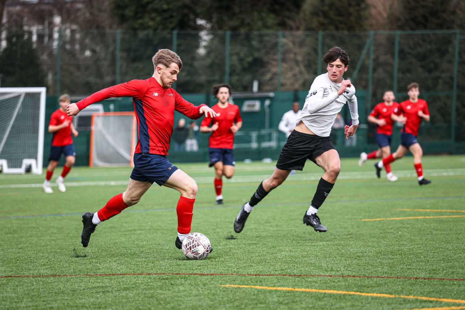 Soccer players competing for the ball during a match on an artificial turf field.