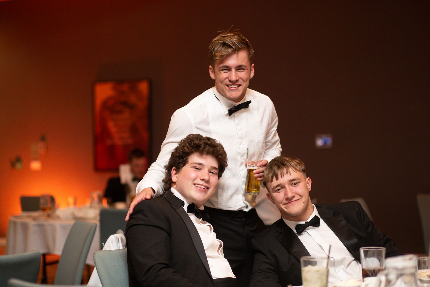 Attendees in formal attire enjoying conversations at an indoor banquet hall.