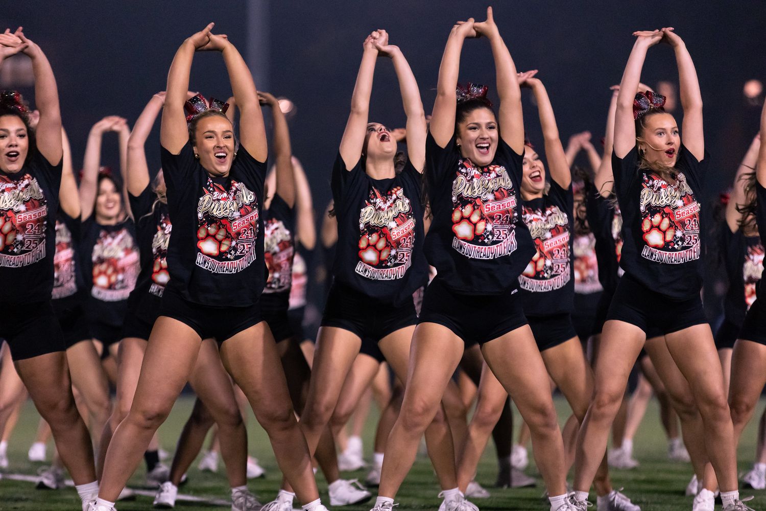 Dance team performs synchronized high kick routine in matching black and red uniforms during halftime show.