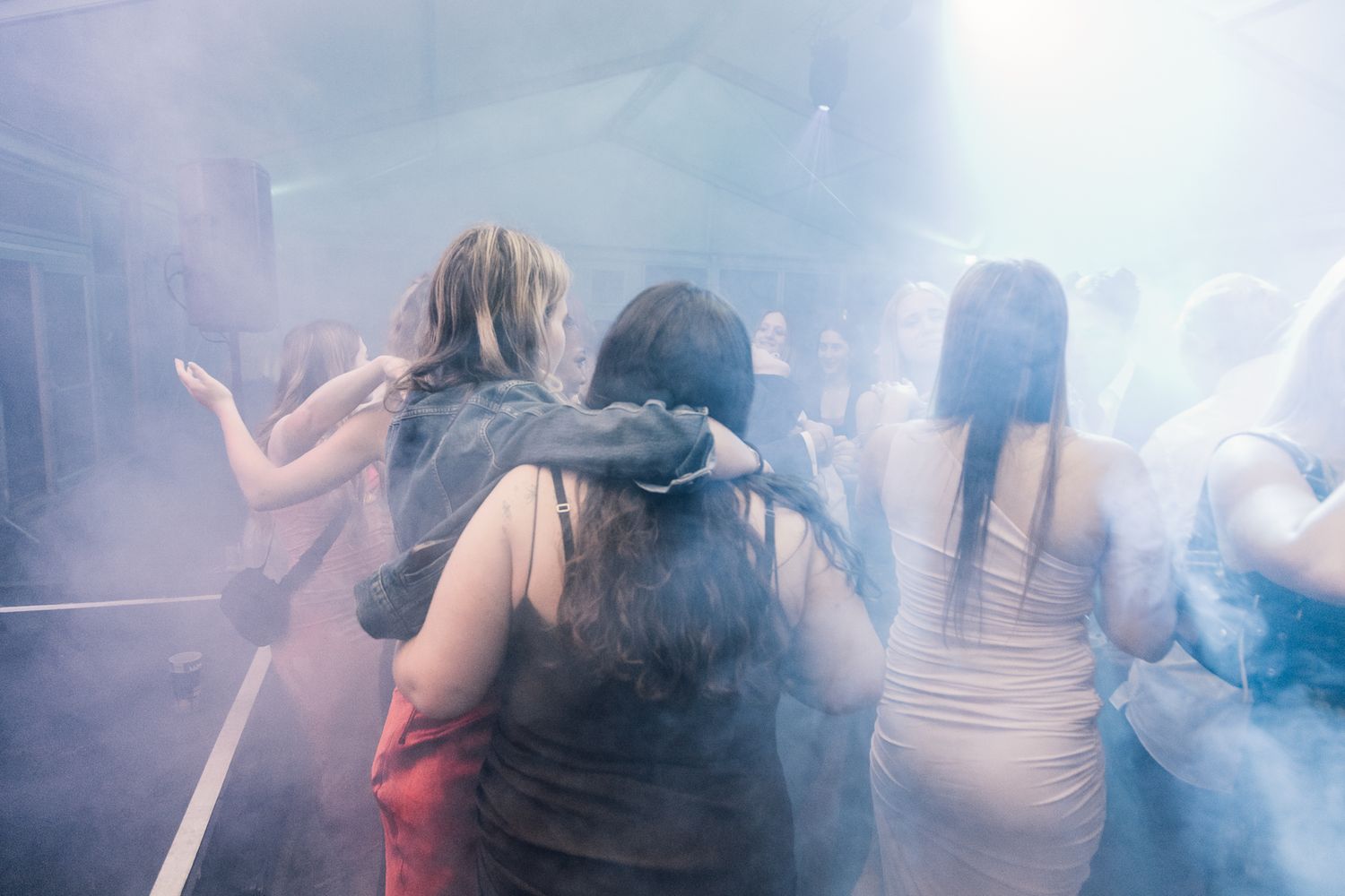 Wedding guests dancing and having fun on a smoke-filled dance floor with atmospheric lighting.