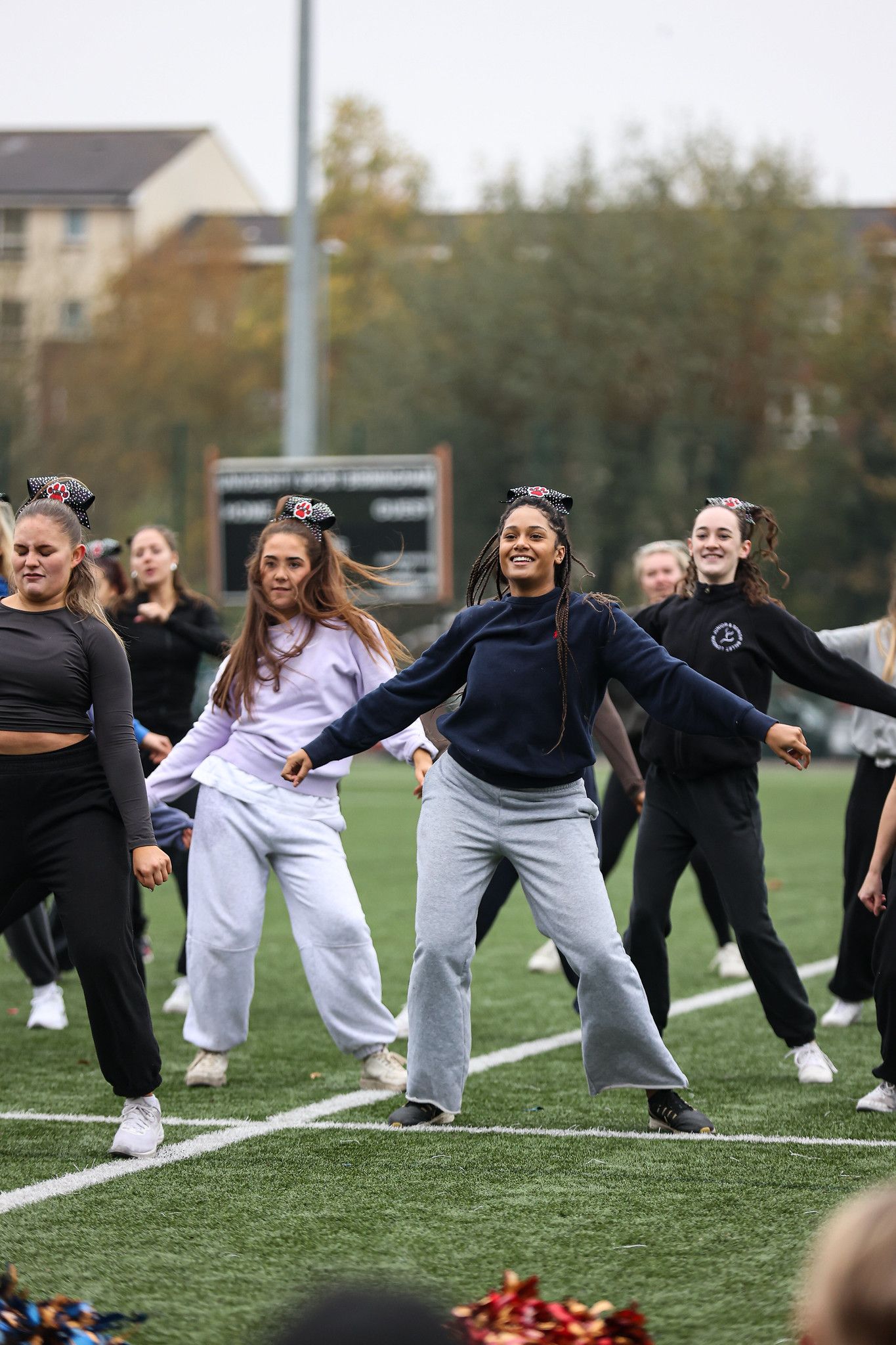Group of dancers performing synchronized movements on an outdoor turf field during practice session.
