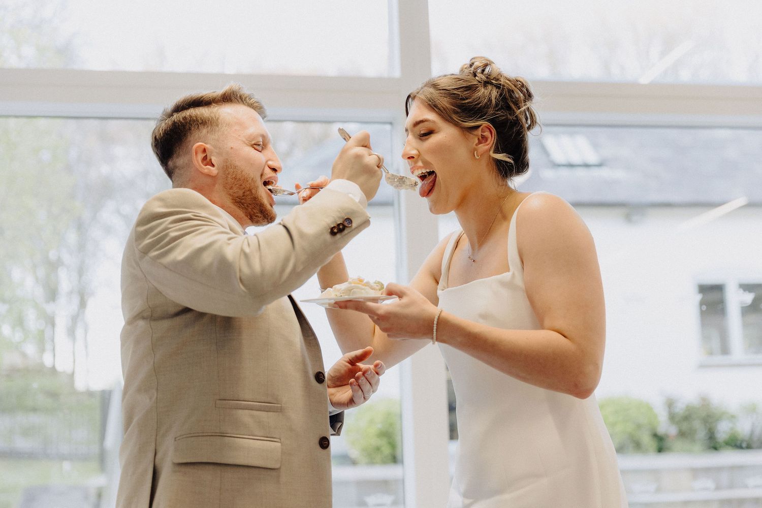 Bride and groom laughing while feeding each other wedding cake at their reception.