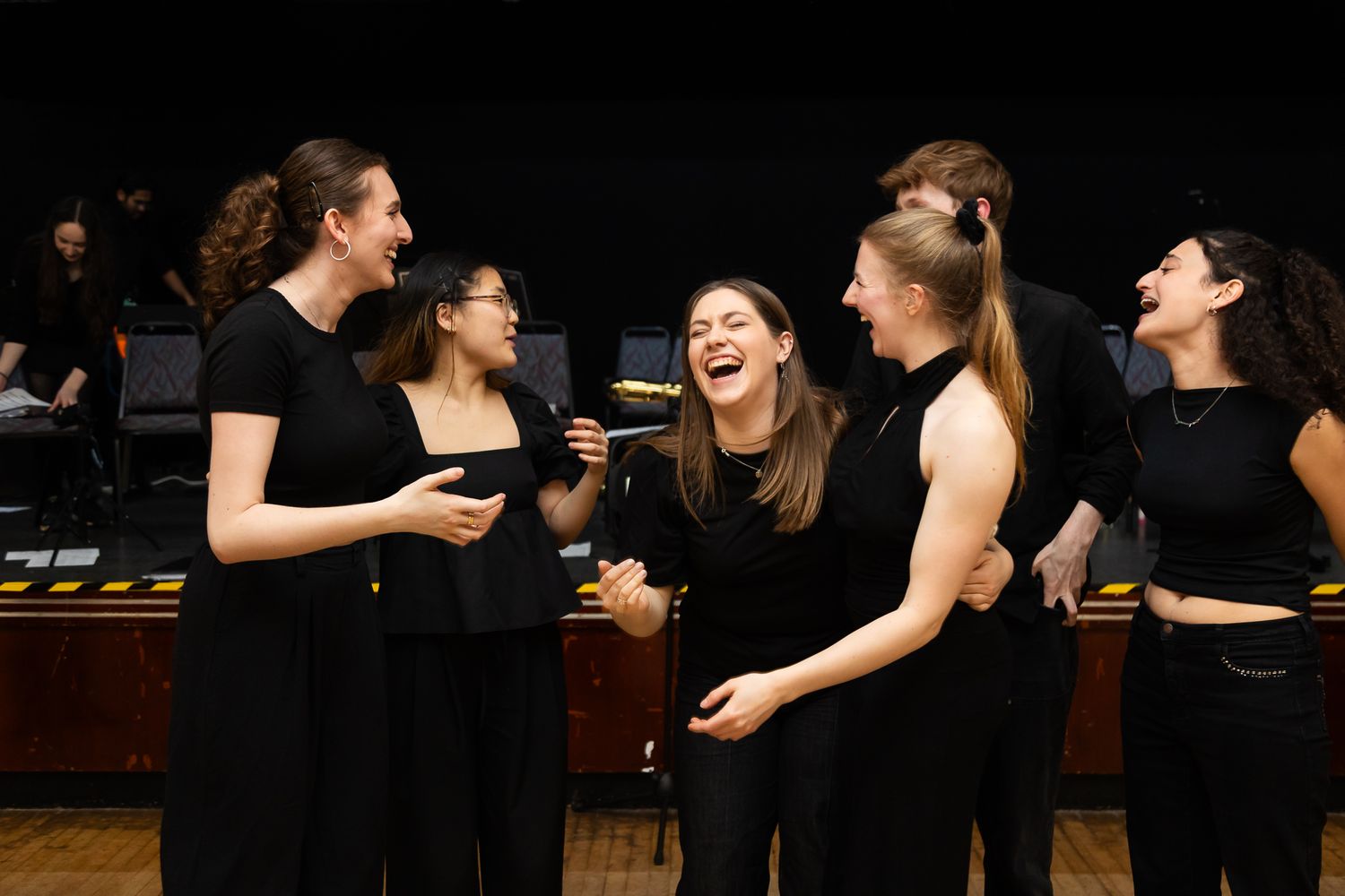 Performers in black attire share a lighthearted moment during a musical performance.