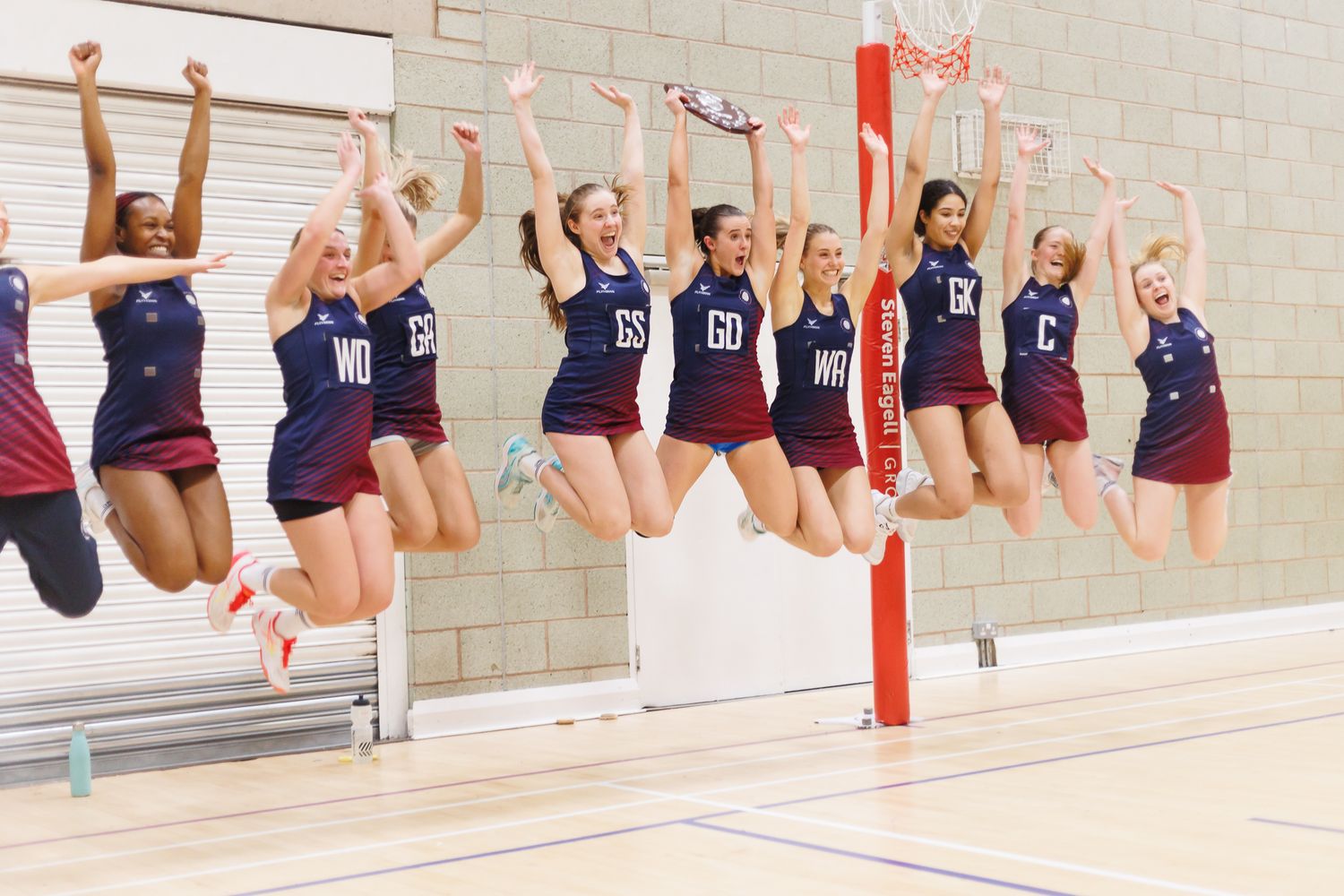 Athletes in athletic uniforms jump simultaneously against a gym wall.