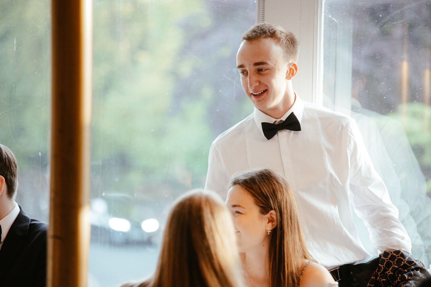 Guests in formal attire mingle at an elegant indoor venue with natural lighting.