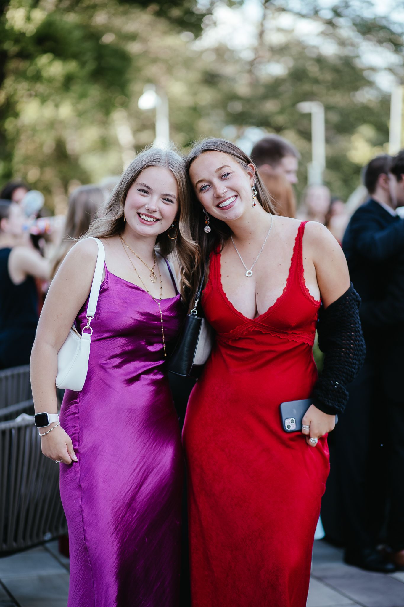 Friends in colorful formal dresses celebrate outdoors at an evening event.