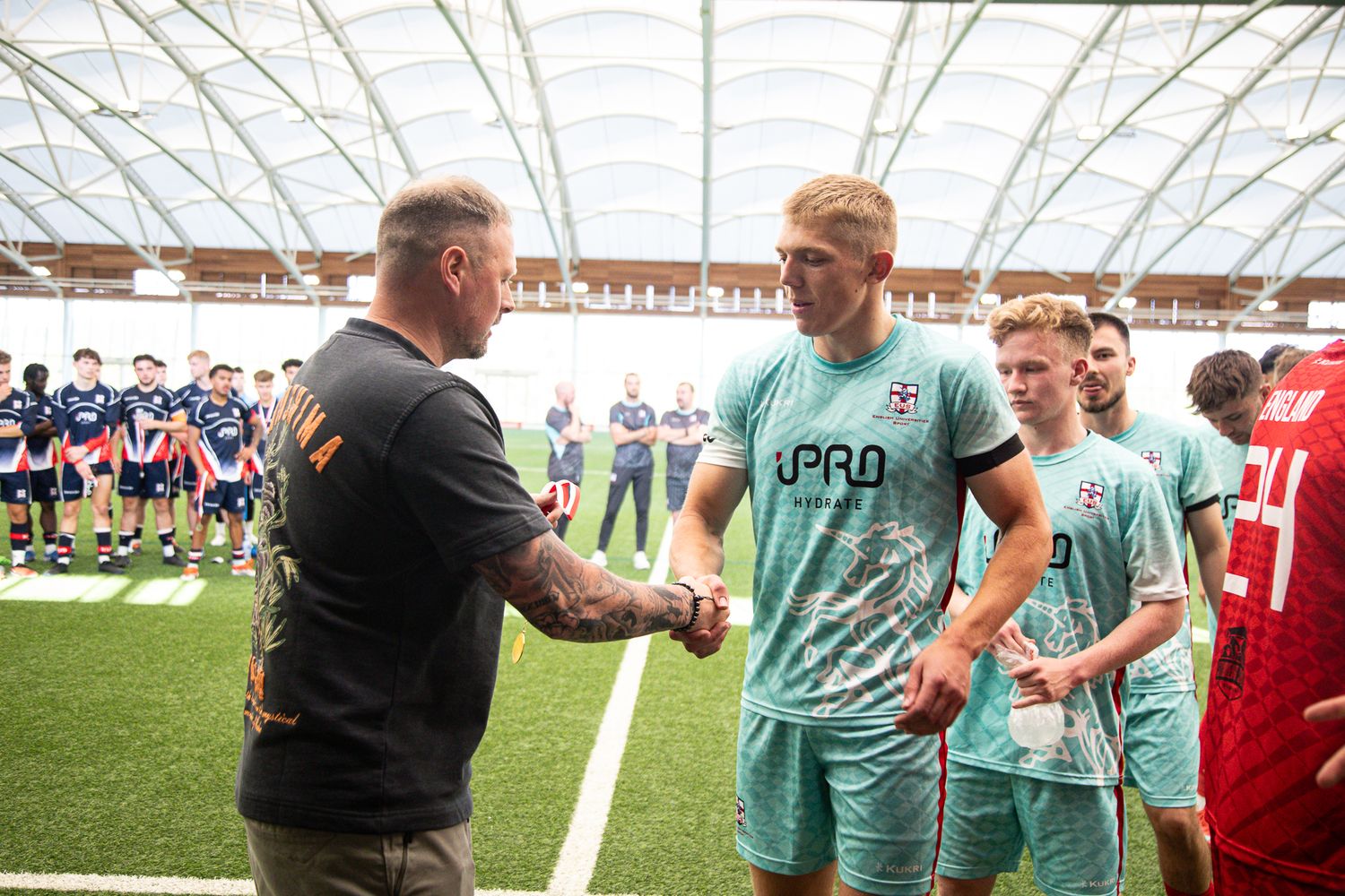 Soccer players and staff interacting during a training session on an indoor field.