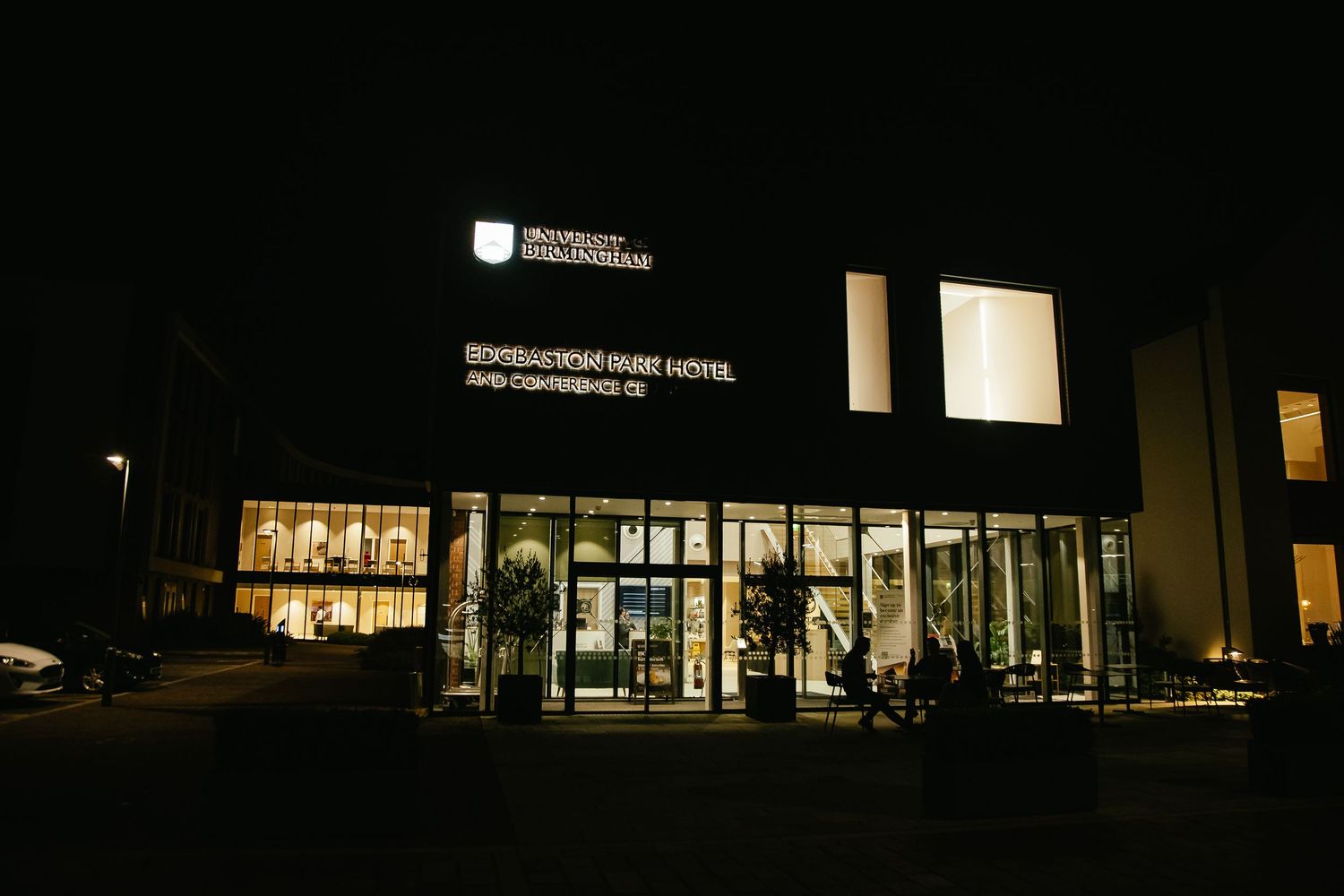 Dark exterior nighttime view of illuminated commercial buildings with glass windows and architectural lighting.