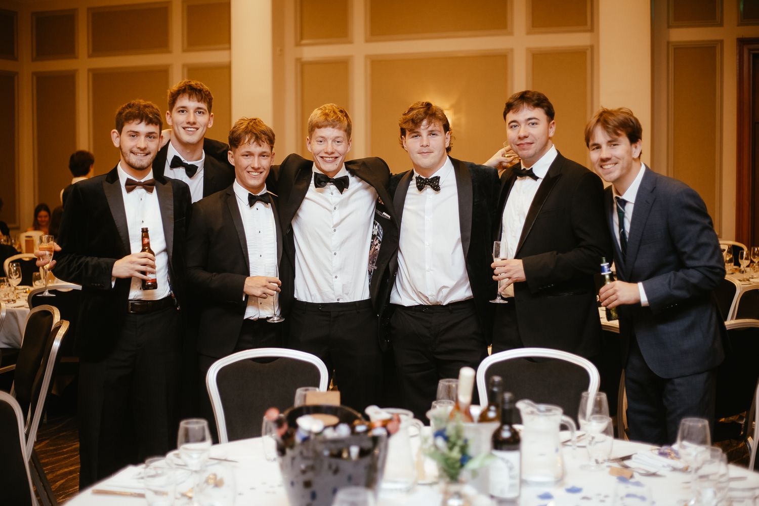 Group of guests in formal attire seated at elegant dining tables during wedding reception.