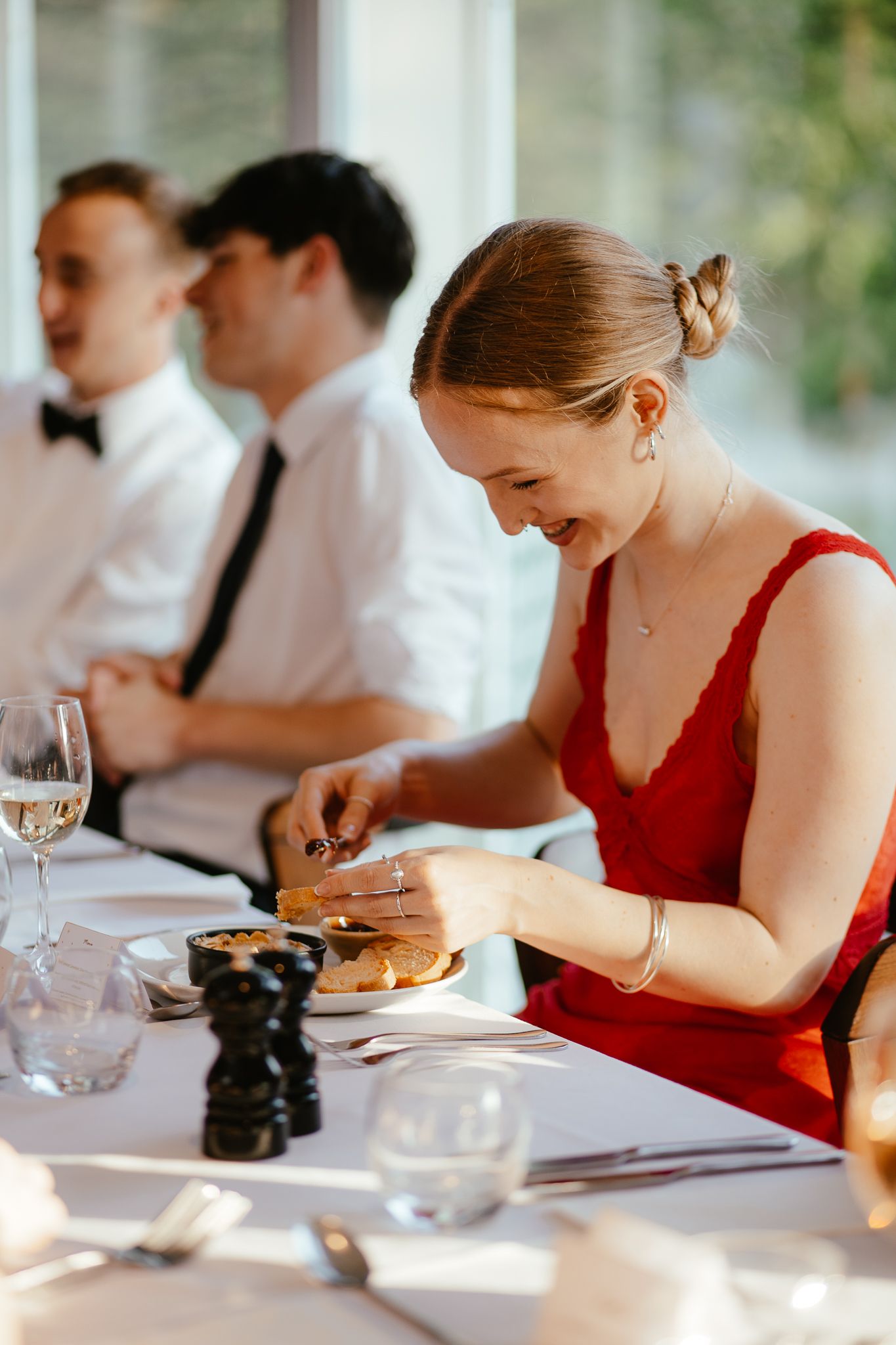 Guests in formal attire dine at an elegantly set table with wine glasses and candles.