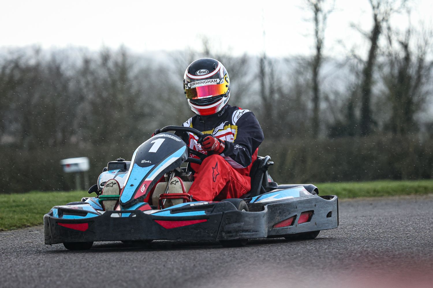 Go-kart racing down a wet track on a cloudy winter day.