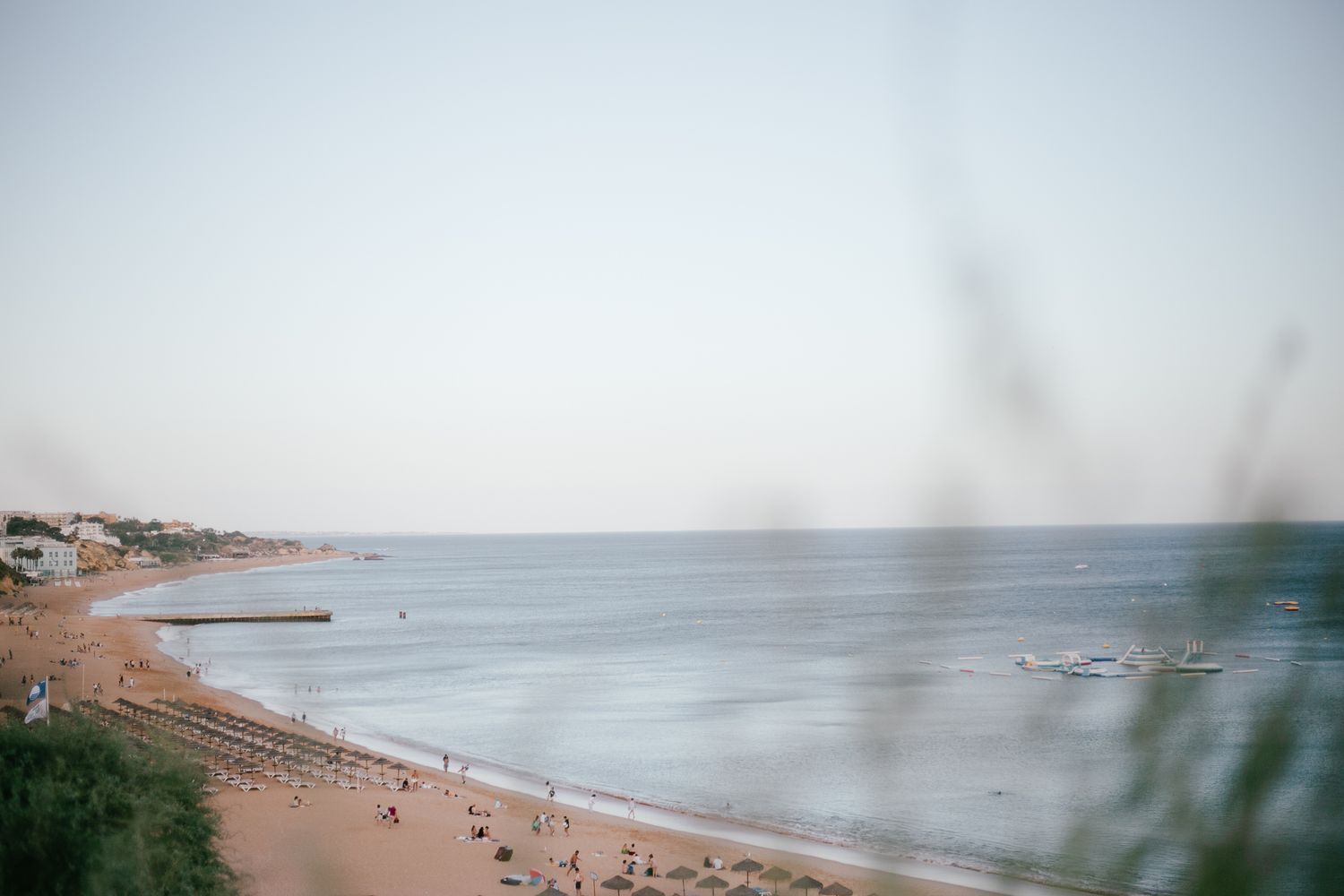 Wide angle view of a serene beachfront with calm waters and scattered beachgoers.