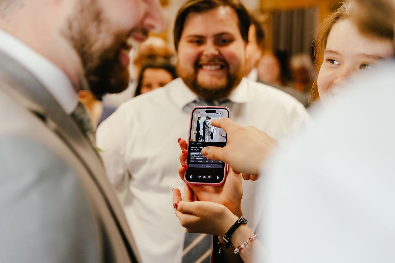 Wedding guest smiles while showing a video on their smartphone during a wedding reception celebration.