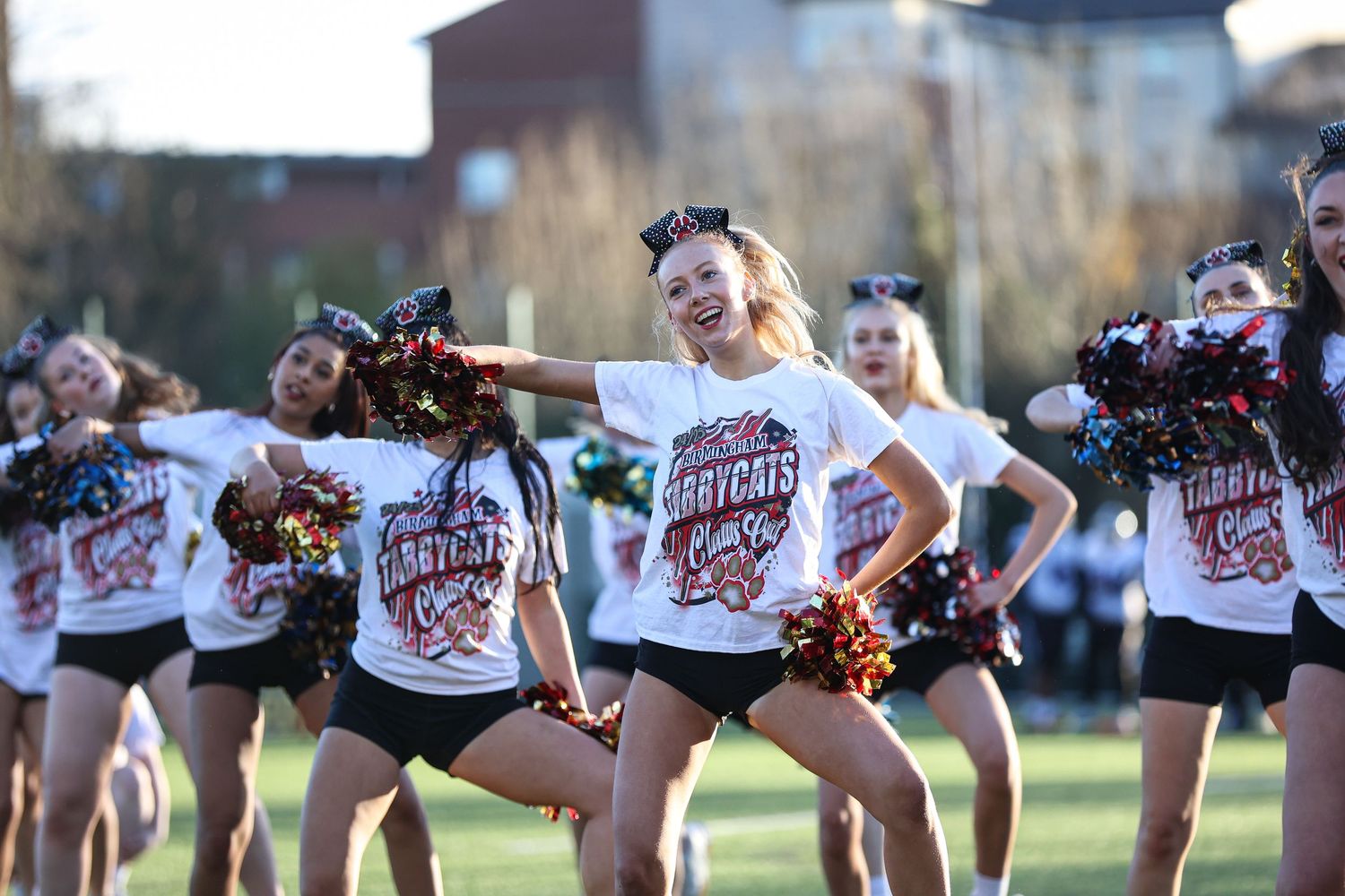Dance team members execute coordinated movements while wearing matching black and white uniforms on a field.