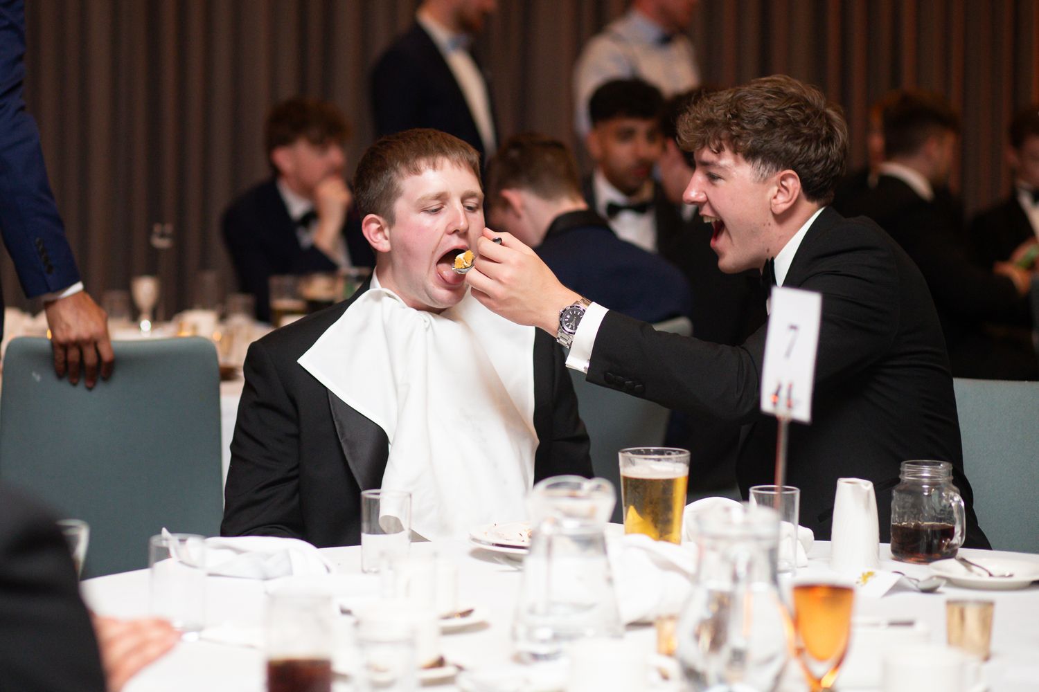 Formal dinner event with guests in black tie attire enjoying conversation at decorated tables.