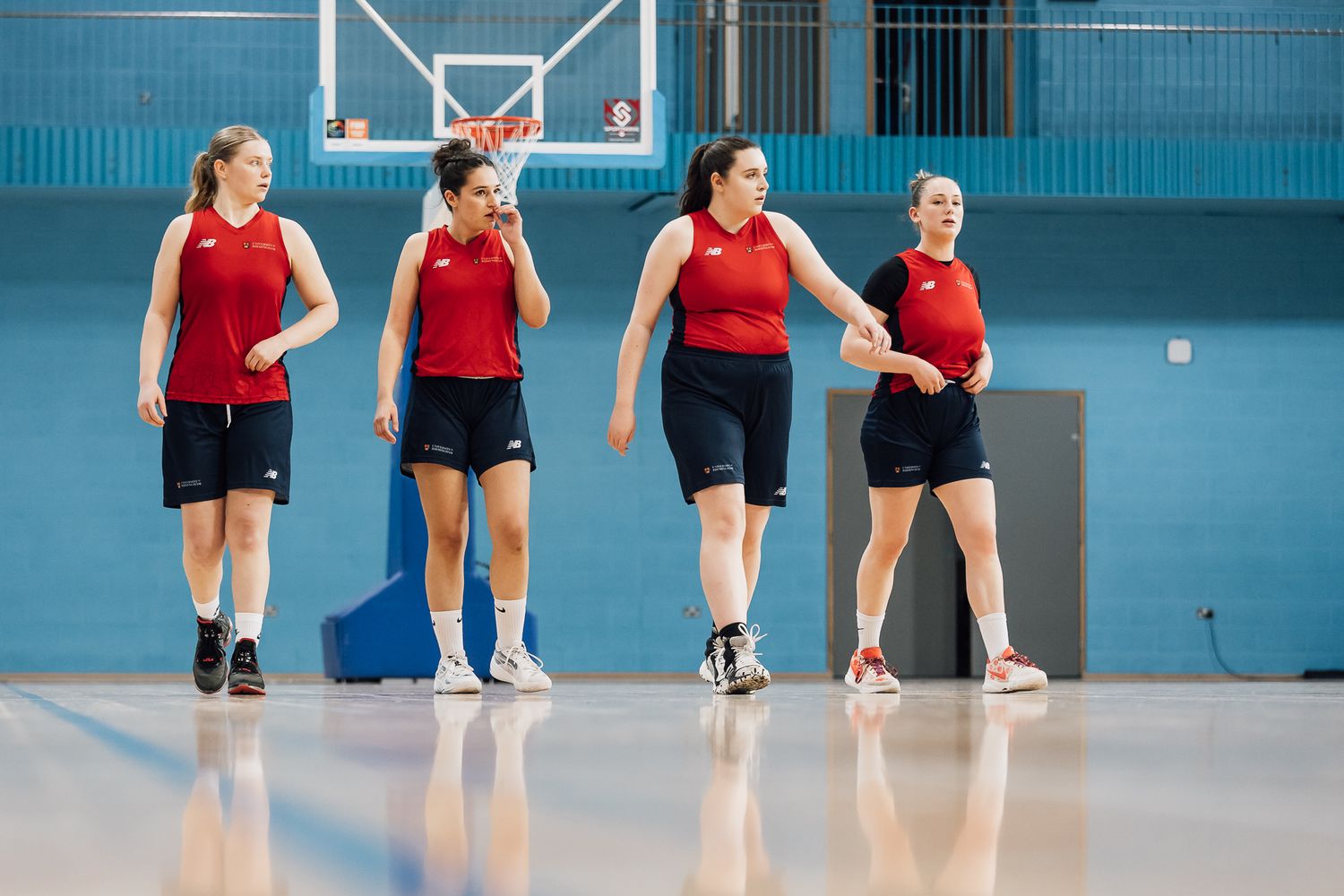 Players performing dynamic warmup exercises in bright indoor gymnasium with blue walls.