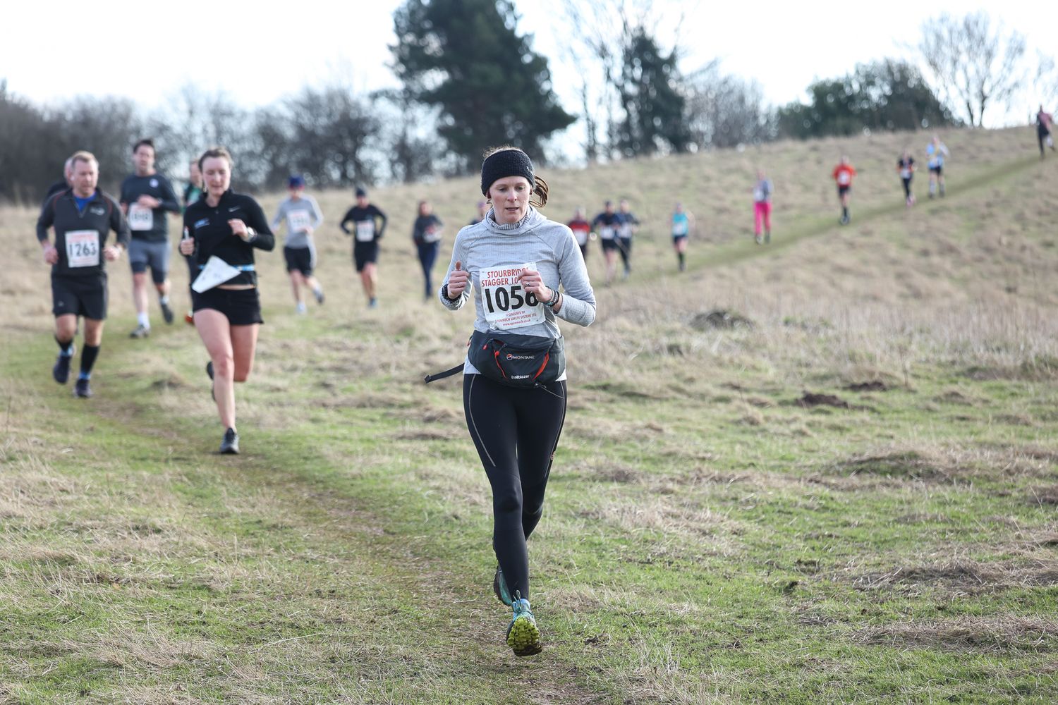 Runners making their way uphill on a grassy cross country course during a race.