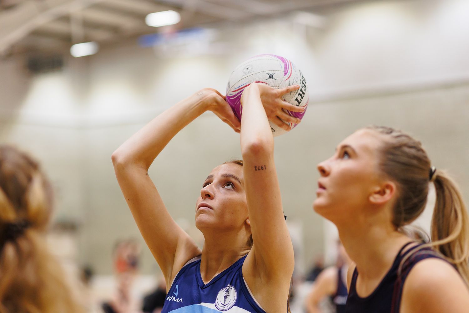 Players jumping high to catch a netball during an indoor match.