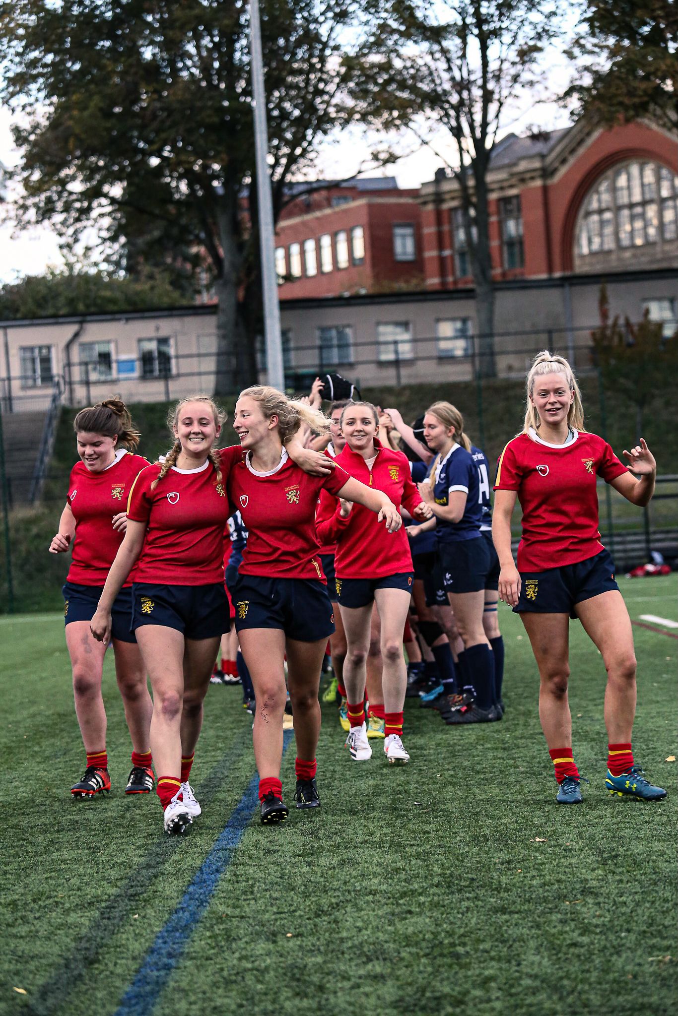 Team of athletes in red uniforms walking together across a sports field.