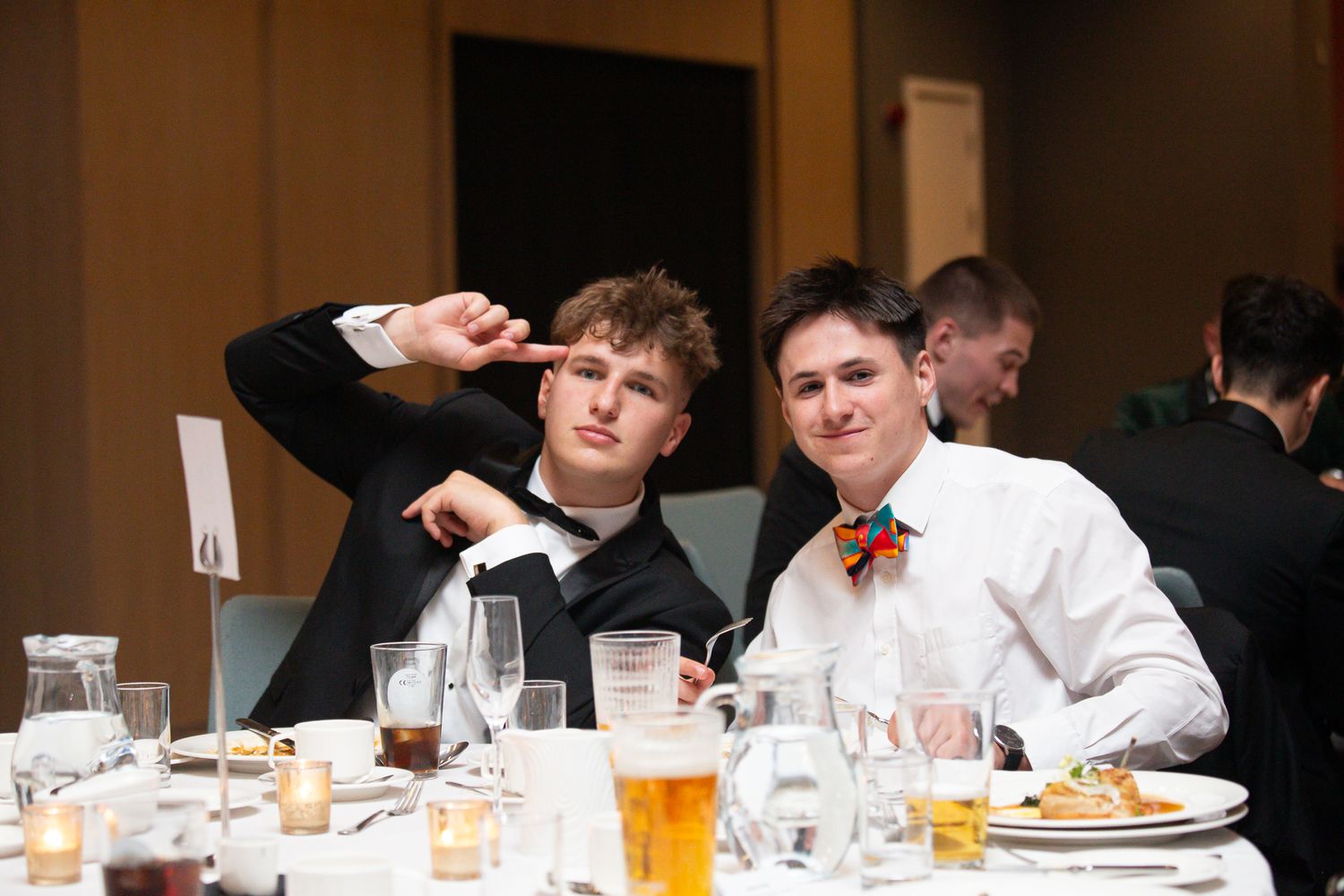 Guests in formal wear seated at banquet tables during an indoor celebration.