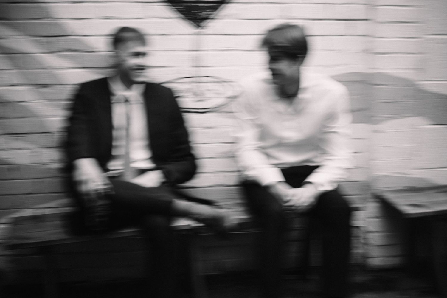 Black and white photograph of party guests posing against a white brick wall.