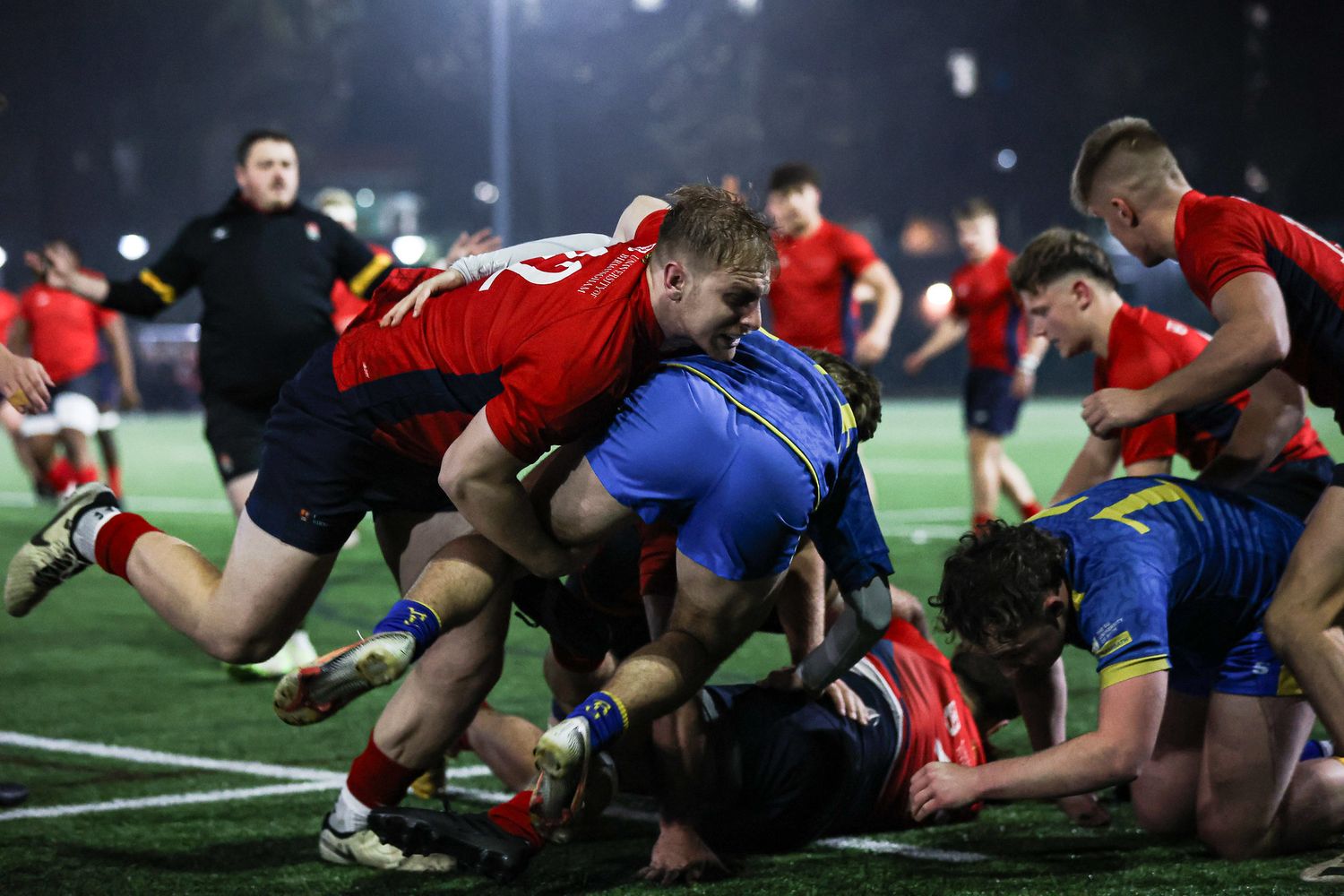 Rugby players engage in a scrum formation during an intense match between teams in red and blue uniforms.