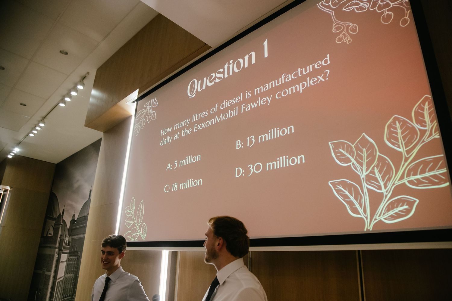 Business presentation slide showing text and floral graphics projected on screen in dimly lit room.