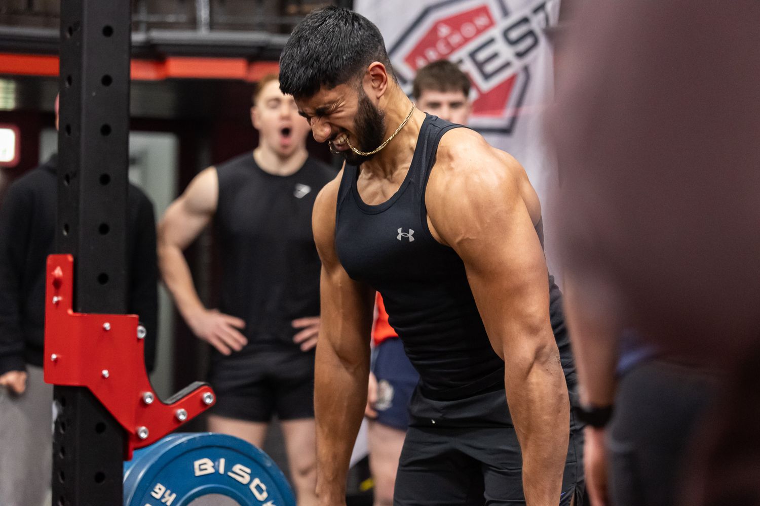 Athletes in black tank tops prepare for weightlifting exercises at a well-equipped gym facility.