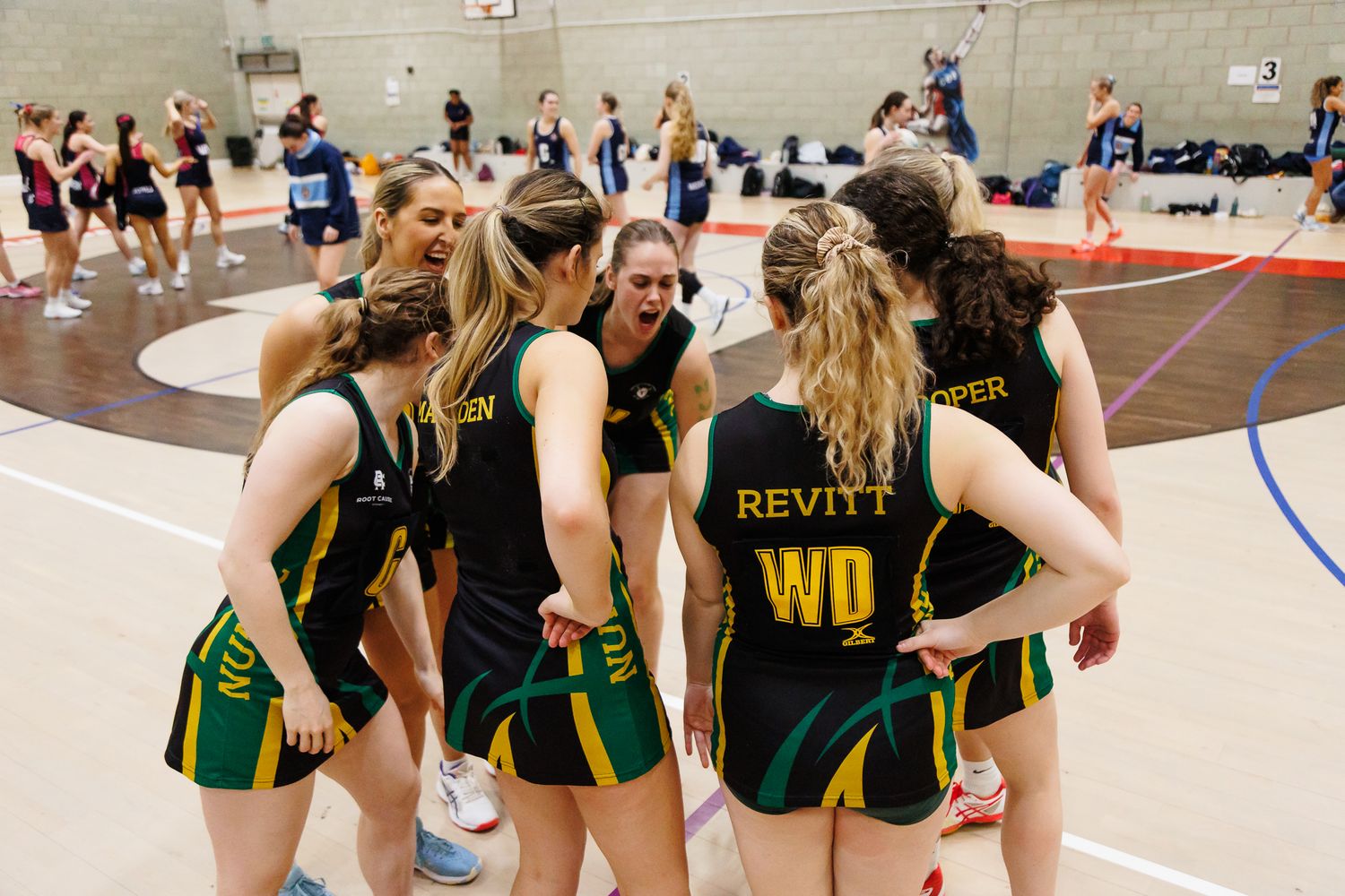 Netball team huddle wearing green and black uniforms during a timeout break.