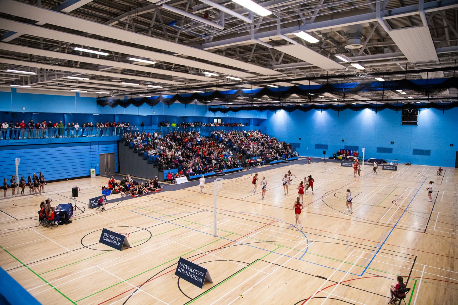 Wide view of an indoor sports facility with blue courts and stadium seating.
