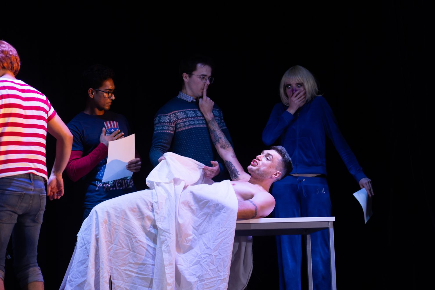Theatrical performance with actors in dramatic lighting on dark stage.
