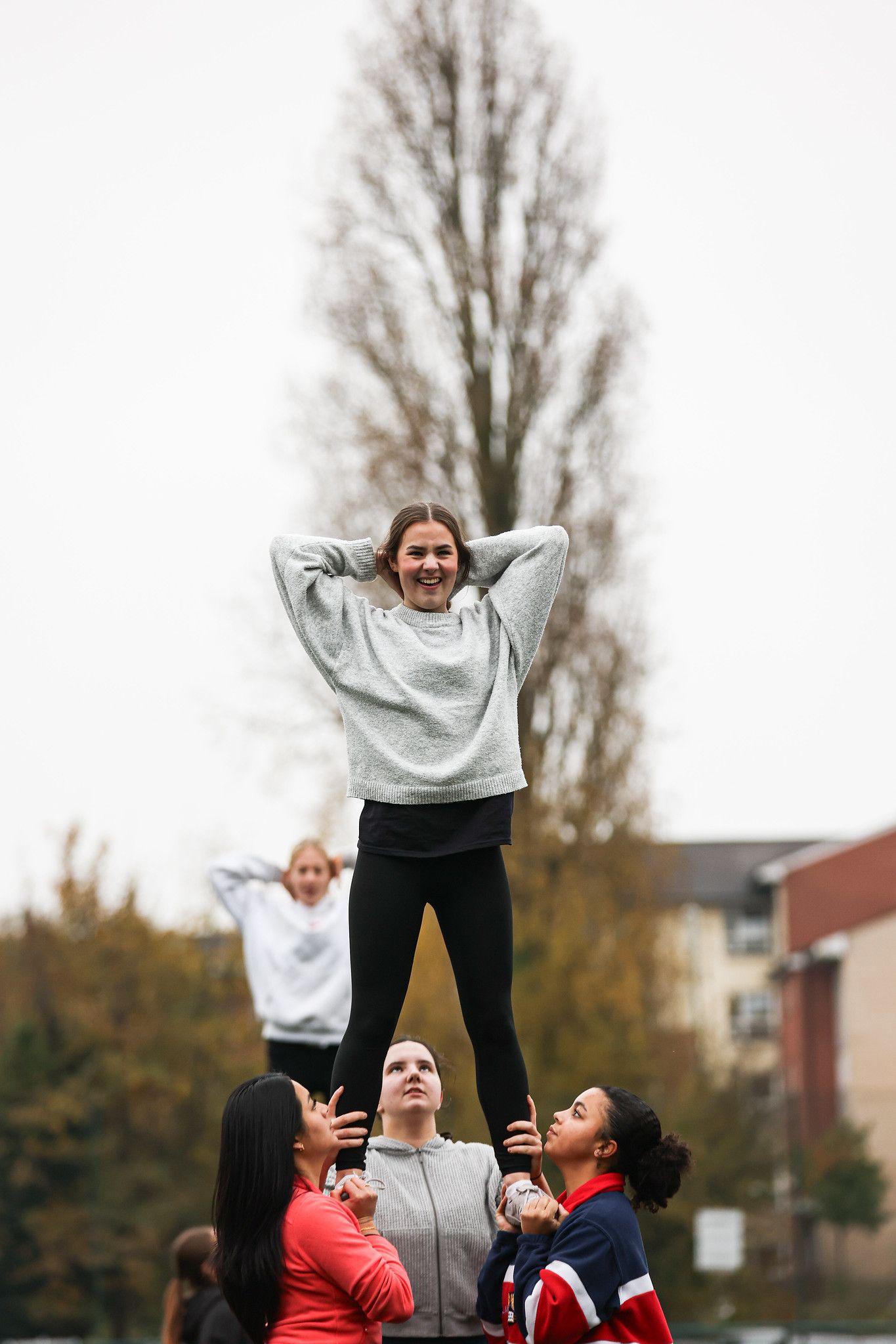 Cheerleaders practicing stunts and lifts outdoors in grey and red uniforms on an autumn day.