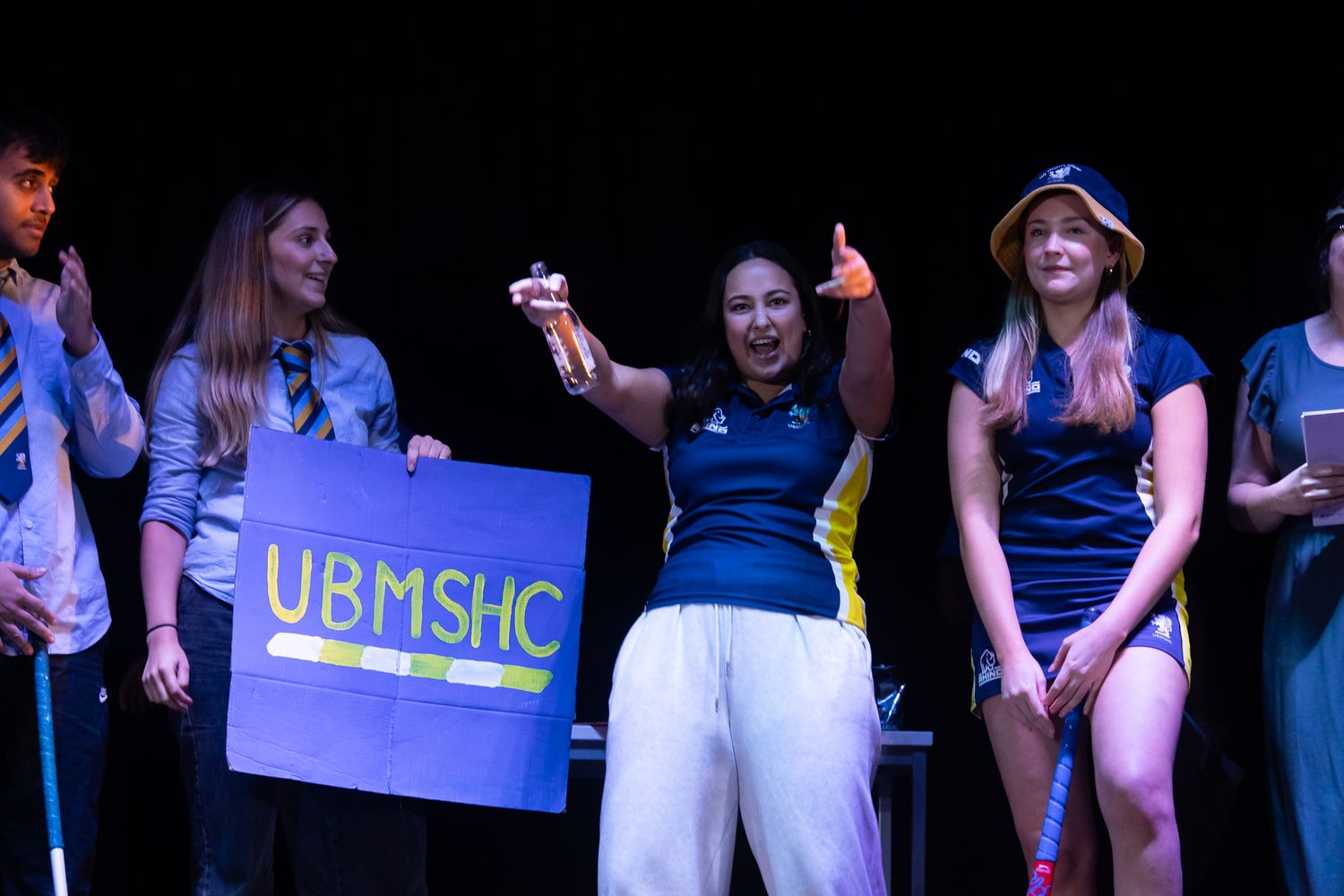 Performance group on stage with UBMSMC banner in blue lighting.