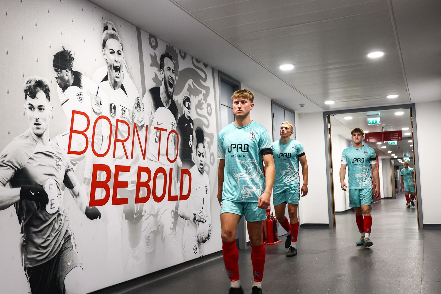 Indoor training facility hallway with motivational text 'BE BOLD' painted on white walls.
