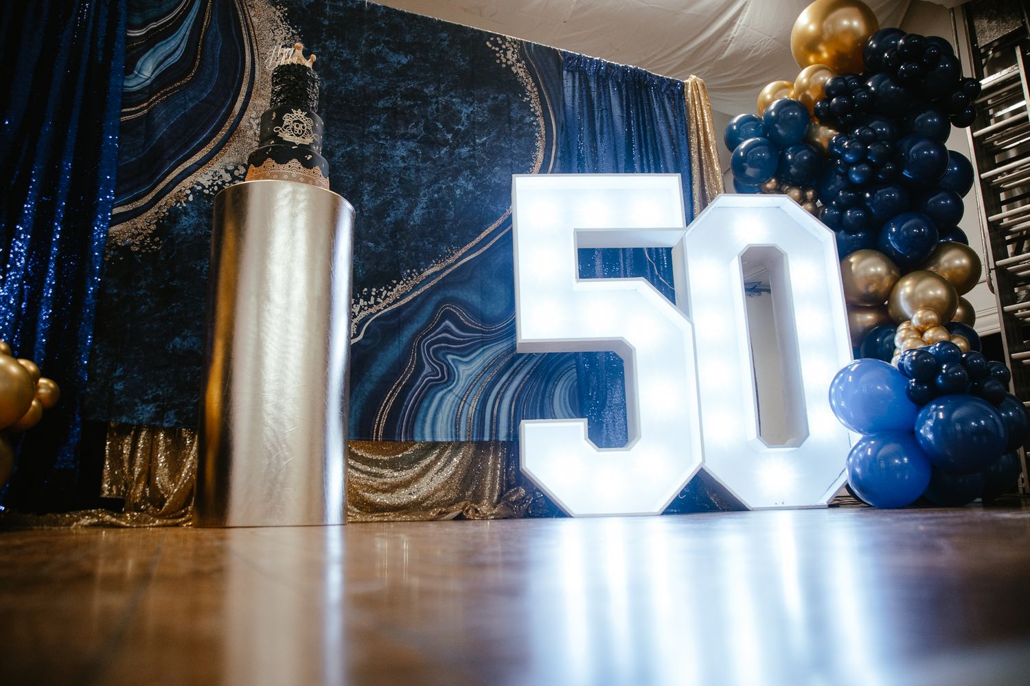 Illuminated number 50 display with blue and gold balloon decorations at an event.