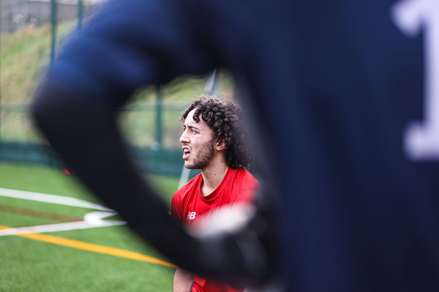 Player in red uniform seen through blurred foreground during sports match.