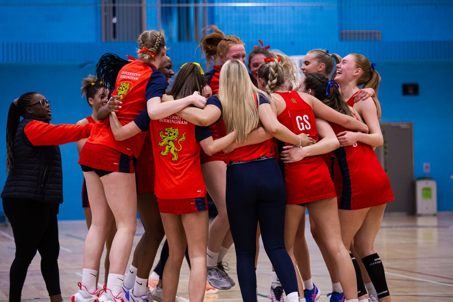Sports team huddle in a blue indoor gymnasium wearing red uniforms.