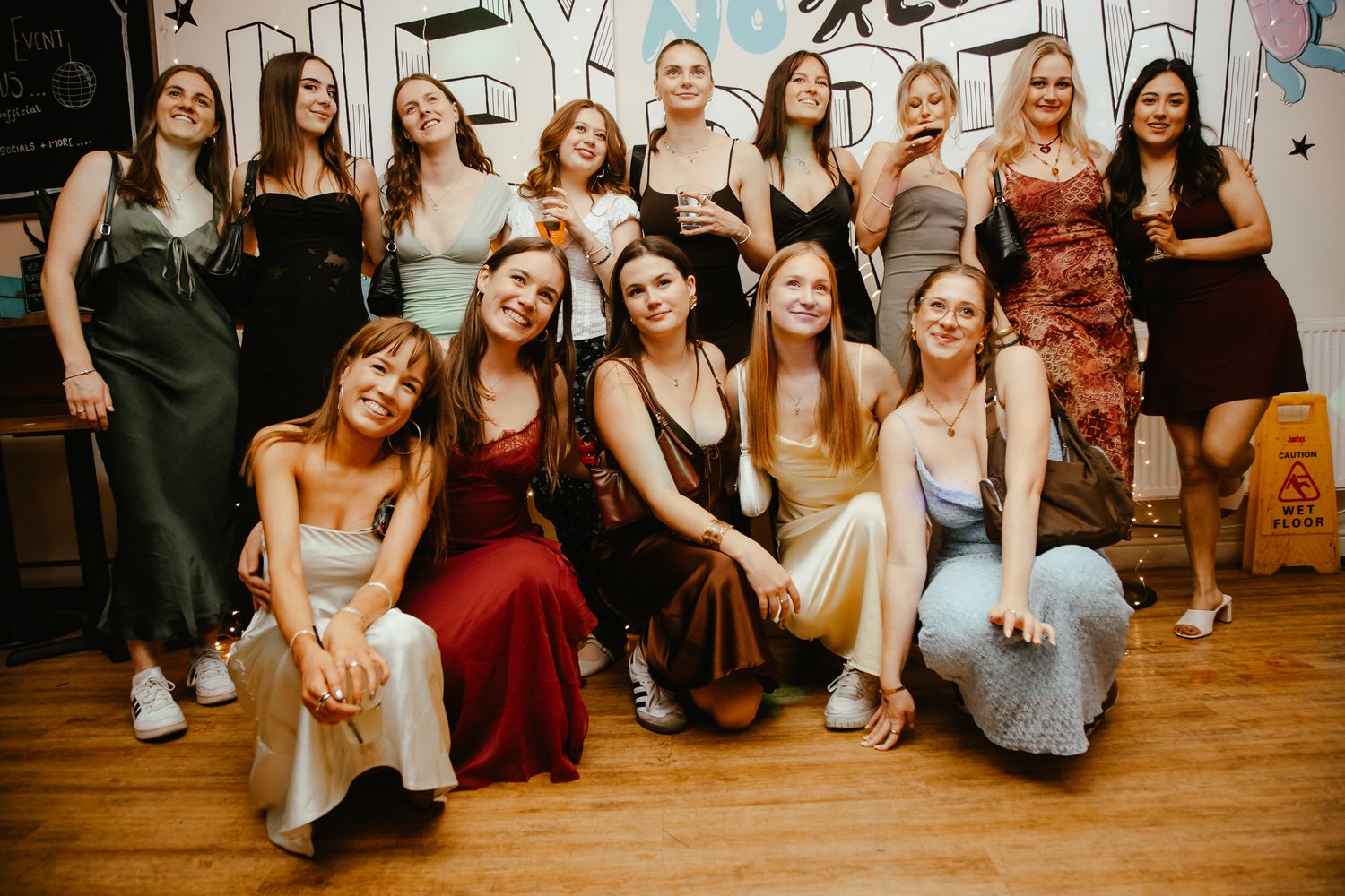 A group of elegantly dressed friends pose together at a party in formal attire and gowns.