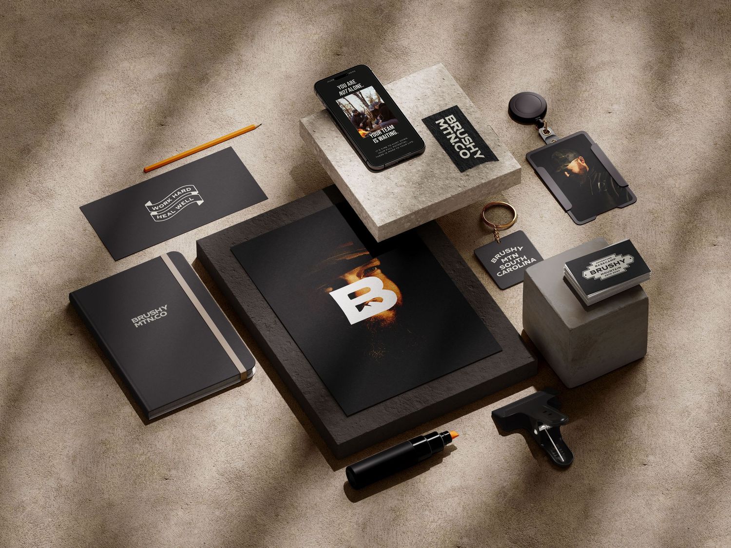 Elegant branded stationery set with black notebooks, phone case, and accessories arranged on a textured surface.