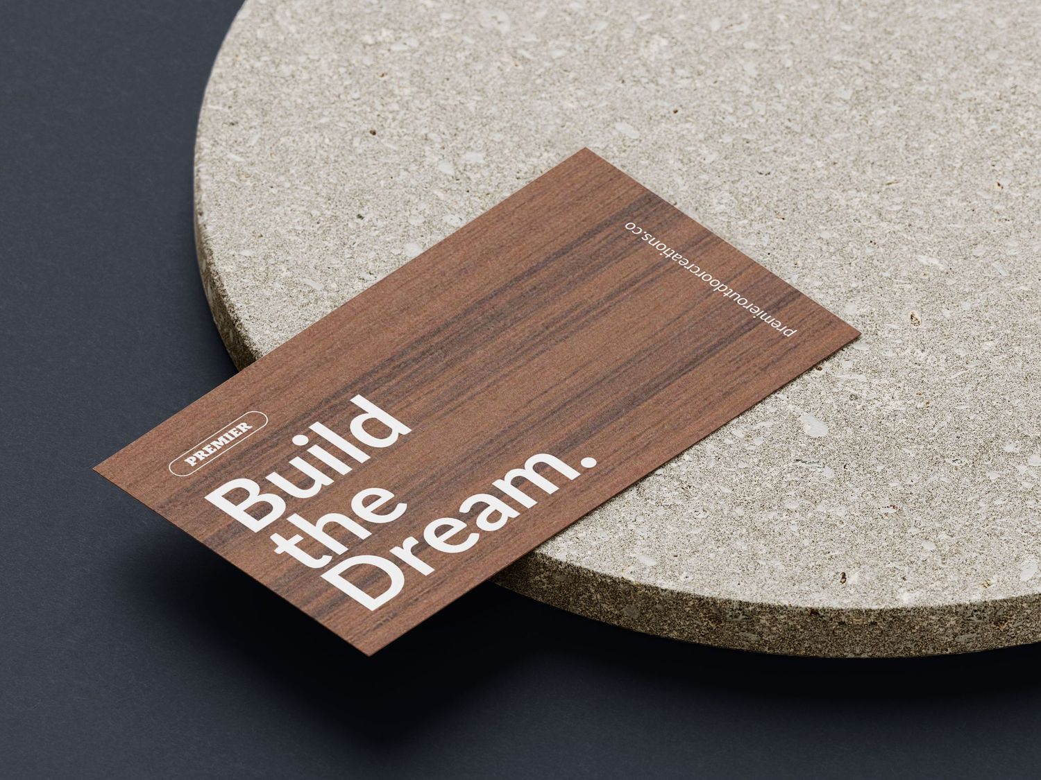 A wooden business card with 'Build the Dream' text resting on a concrete surface, showcasing elegant branding design.