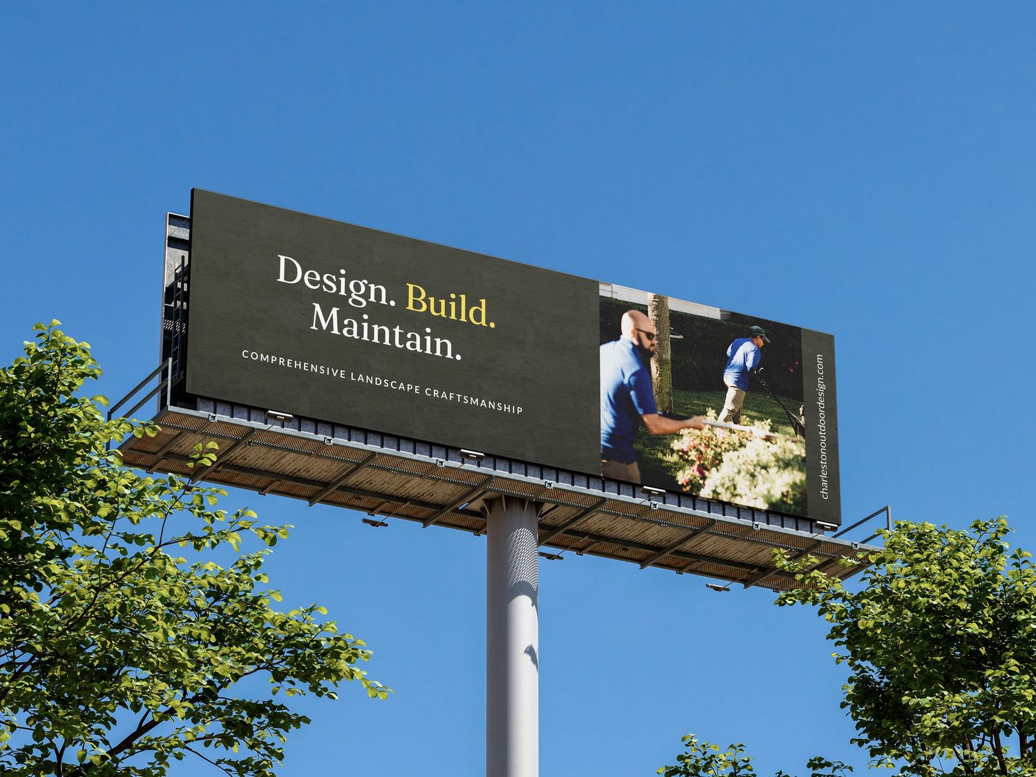 Billboard against blue sky reading Design Build Maintain for a landscape company, surrounded by green trees.