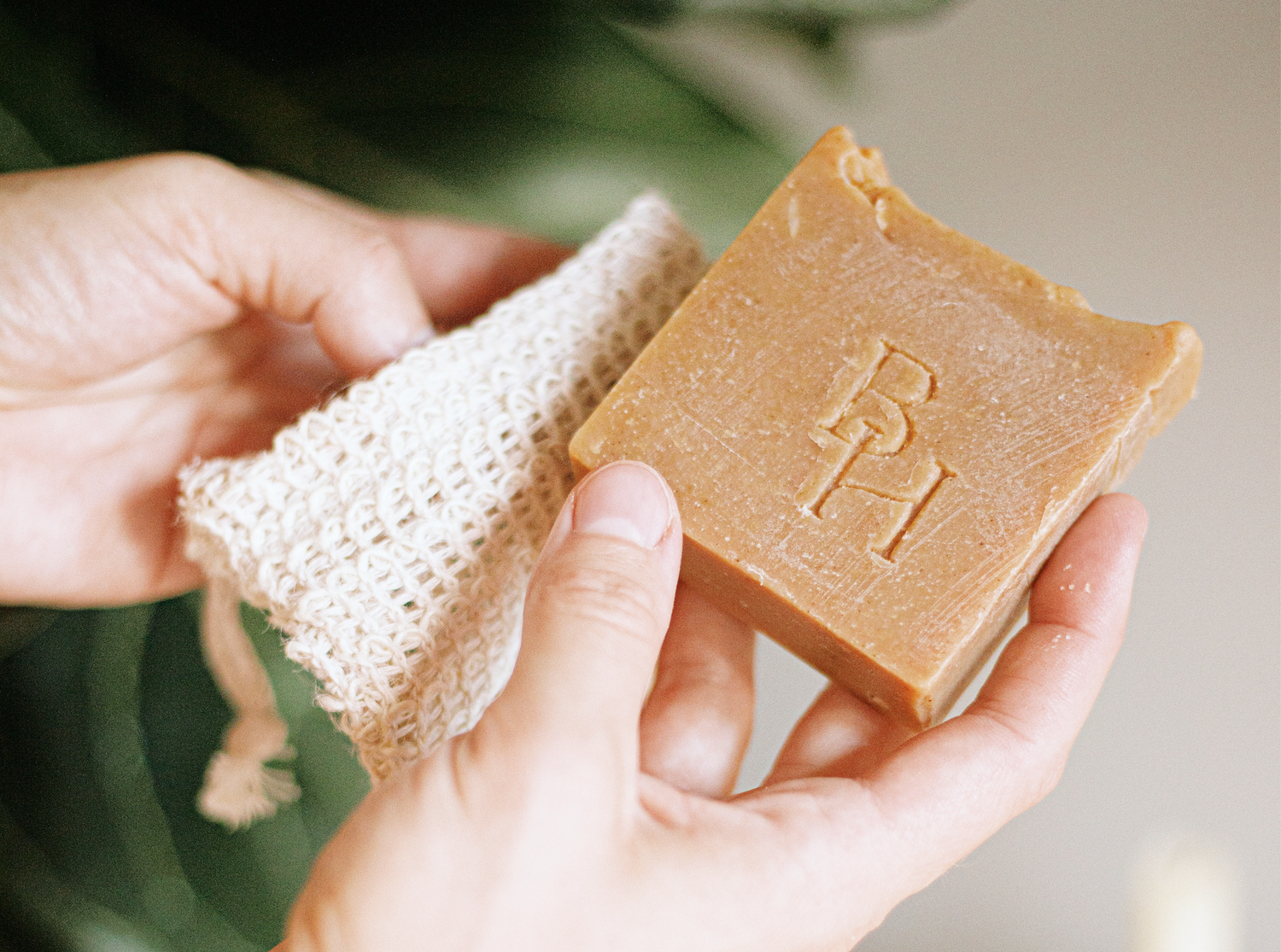 Hands holding a handmade natural bar soap with embossed logo next to a textured sisal exfoliating cloth.