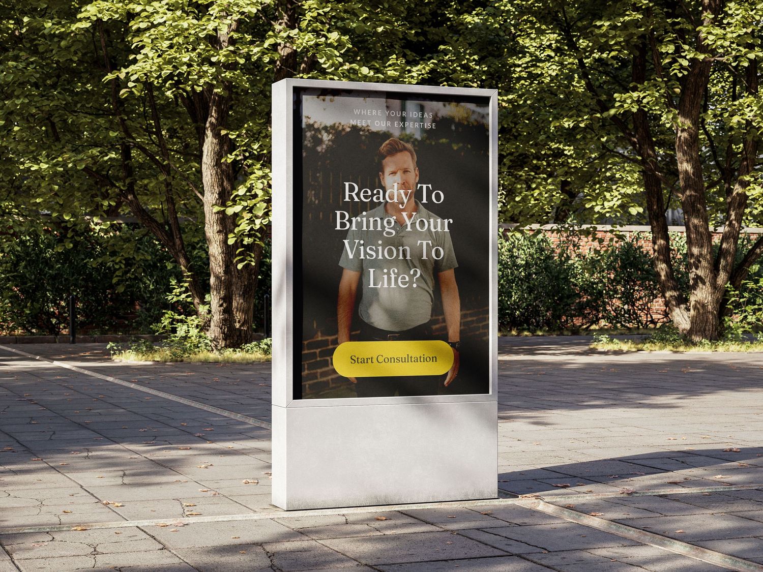 Outdoor digital billboard displaying 'Ready To Bring Your Vision To Life?' advertisement on a tree-lined sidewalk.
